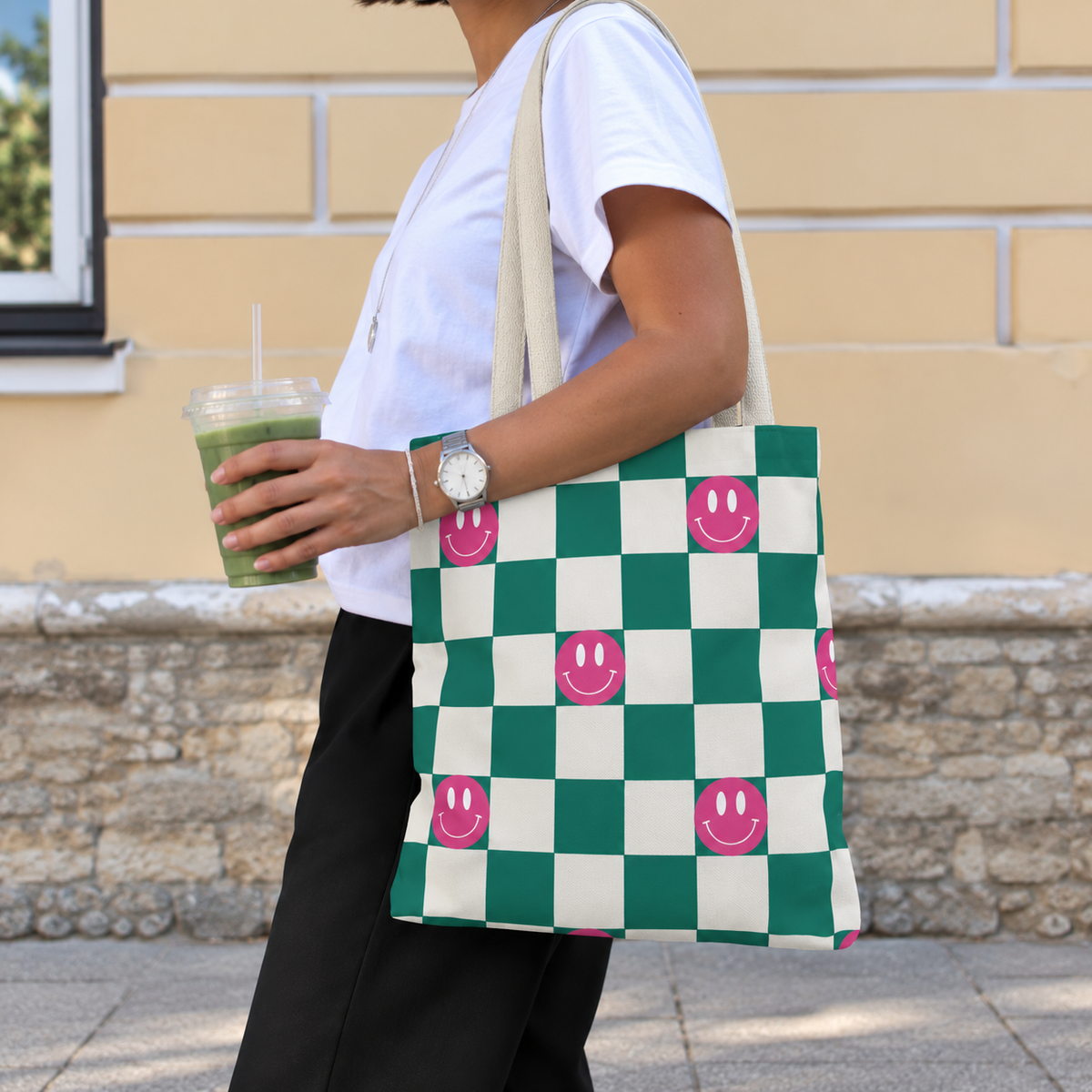 Woman with an iced drink wearing the green smiley checkered tote bag