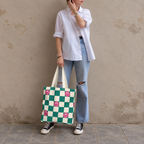Woman in a white shirt and jeans standing with the green smiley checkered tote bag