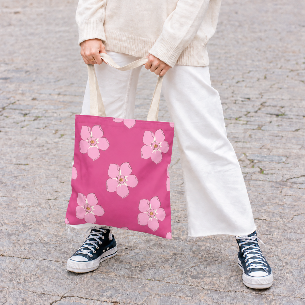 Model in white trousers holding the hot pink floral tote bag