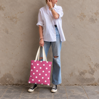 Woman in a white shirt and jeans holding the hot pink polka dot tote bag