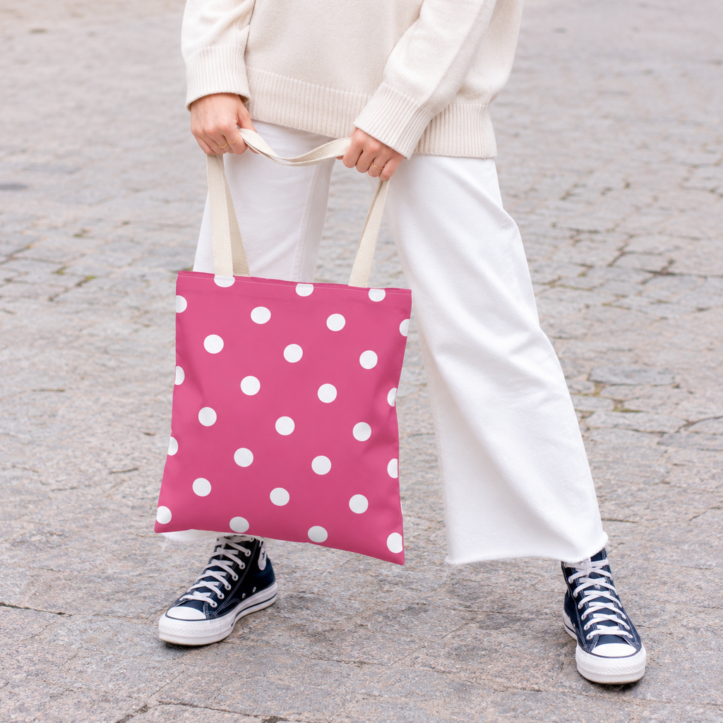 Woman in white trousers and sneakers holding the hot pink polka dot tote bag