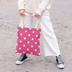Woman in white trousers and sneakers holding the hot pink polka dot tote bag