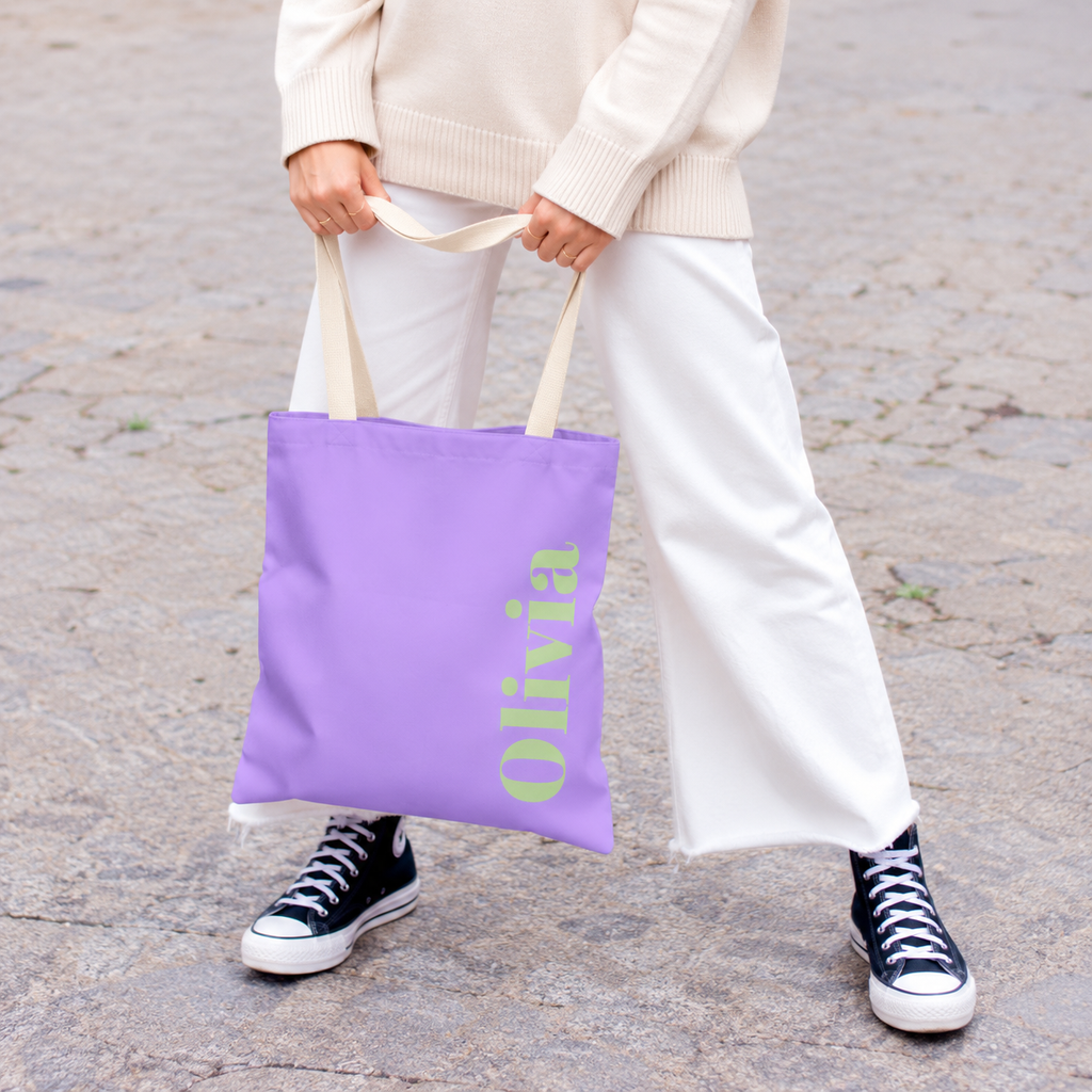 Model holding the Lavender Green Name personalized tote bag in front of white trousers