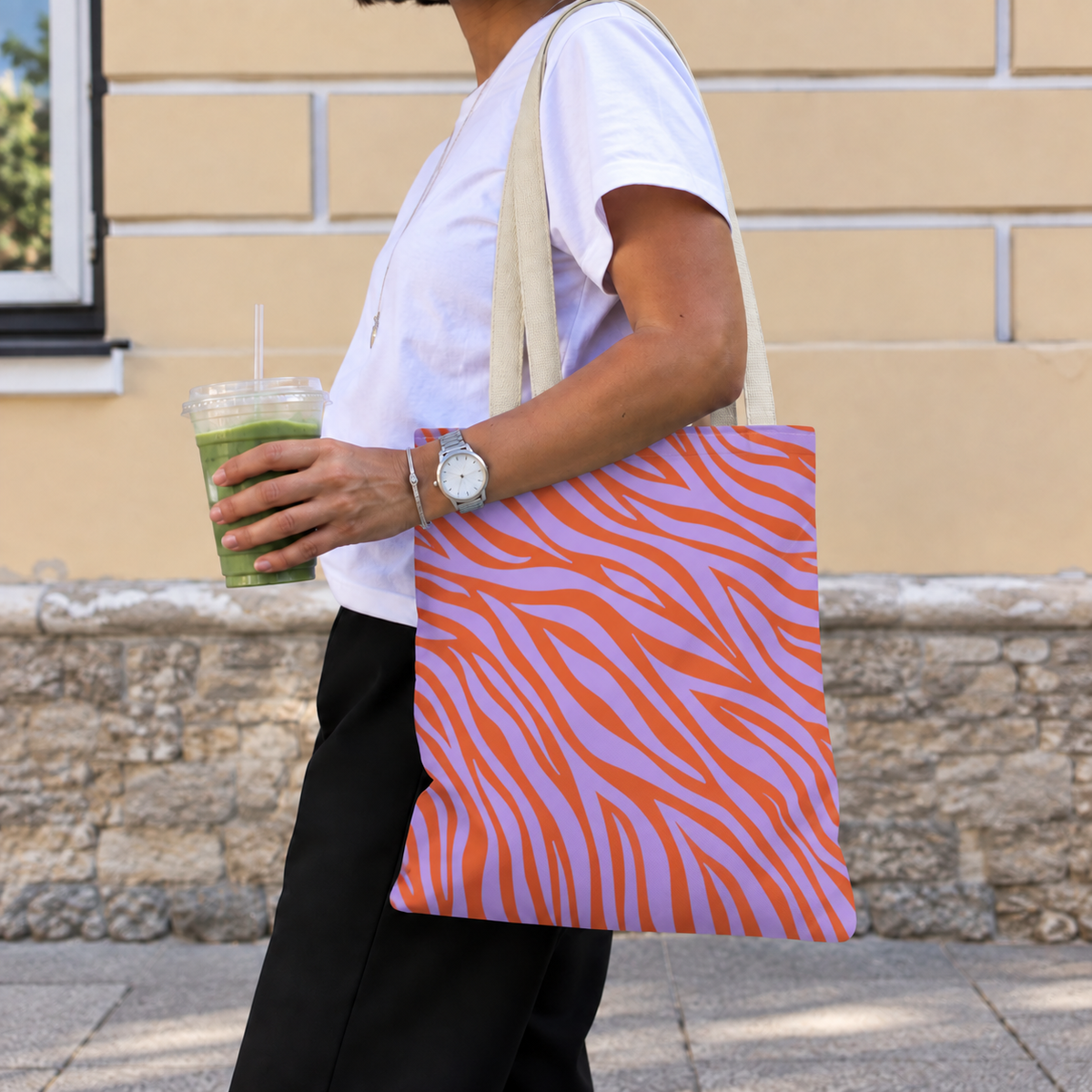 Woman walking with the lavender orange zebra print tote bag on her shoulder and an iced drink