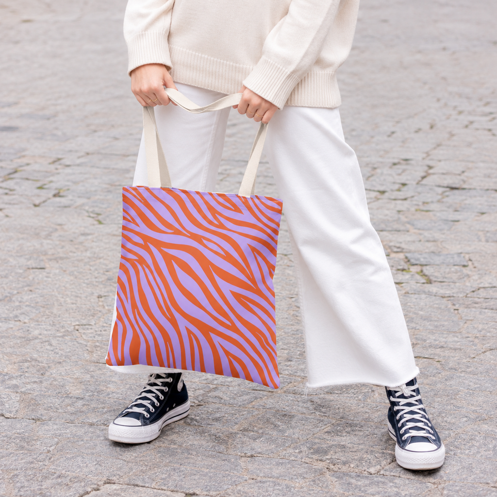 Woman in white trousers and sneakers holding the lavender orange zebra print tote bag