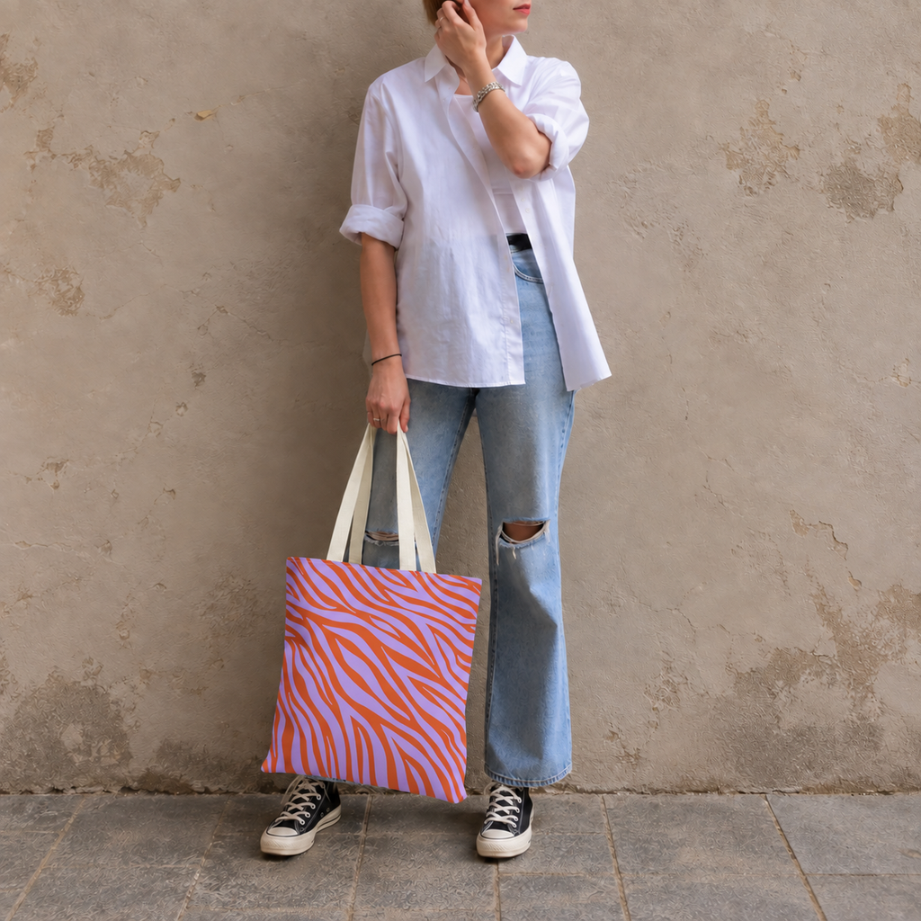 Woman in a white shirt and jeans holding the lavender orange zebra print tote bag