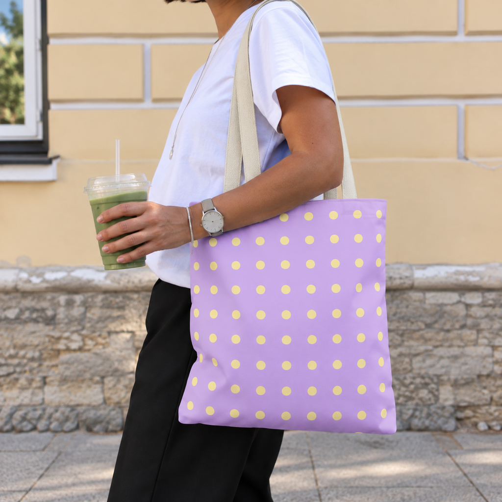 Woman walking with the lavender yellow polka dot tote bag on her shoulder and an iced drink