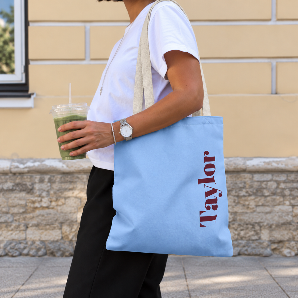 Woman carrying the Light Blue Burgundy Name personalized tote bag, side view with an iced drink
