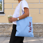 Woman carrying the Light Blue Burgundy Name personalized tote bag, side view with an iced drink