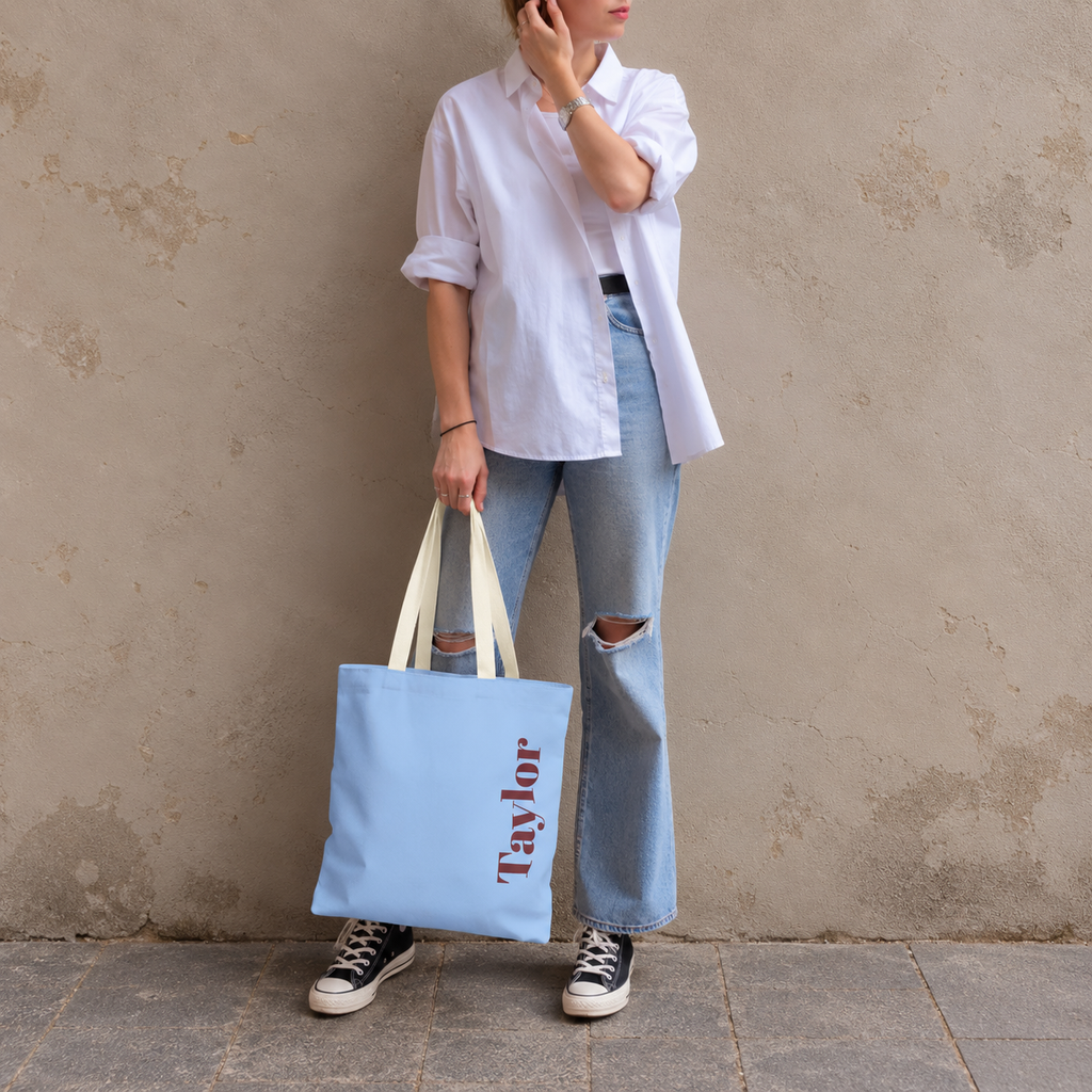 Model standing outdoors with the Light Blue Burgundy Name personalized tote bag in a full-body photo