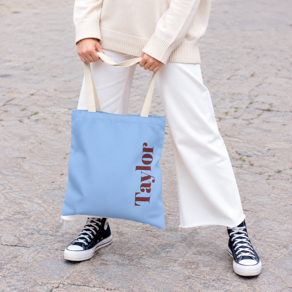 Model holding the Light Blue Burgundy Name personalized tote bag in front of white trousers