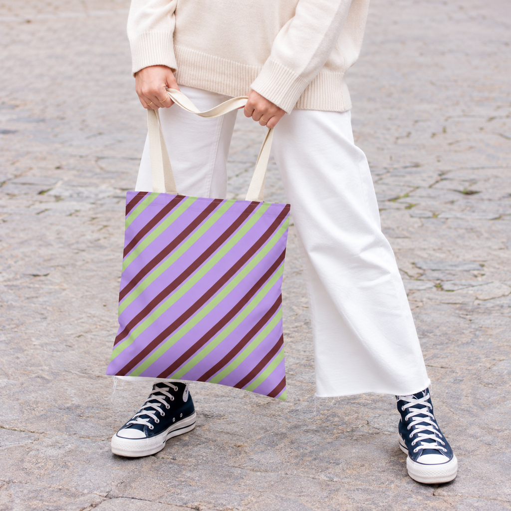 Woman in white trousers and sneakers holding the lilac green striped tote bag