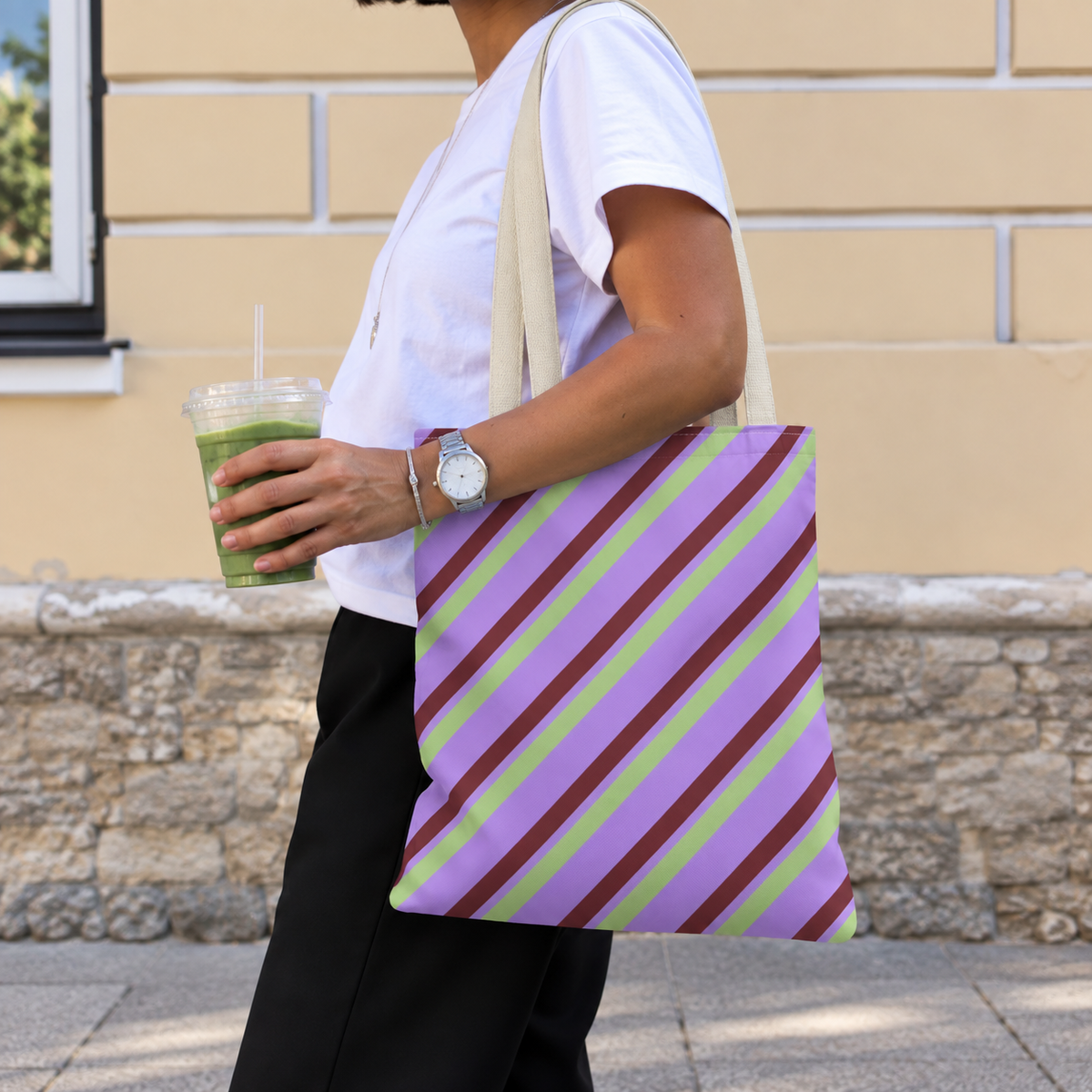 Woman walking with the lilac diagonal striped tote bag on her shoulder and an iced drink