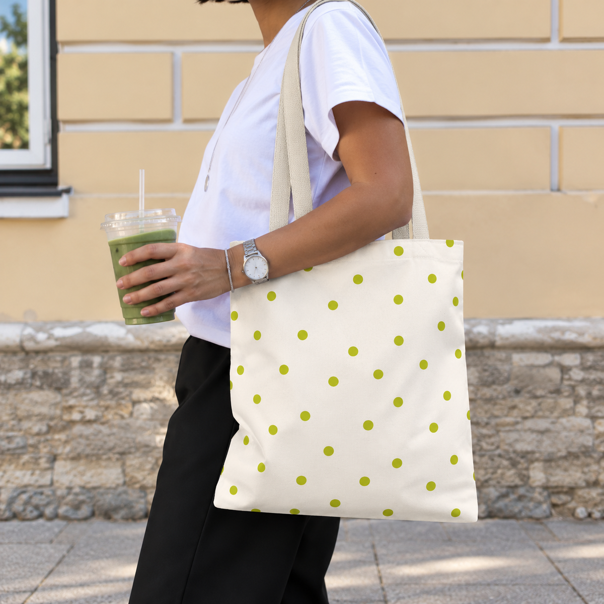 Woman walking with the lime green polka dot tote bag on her shoulder and an iced drink