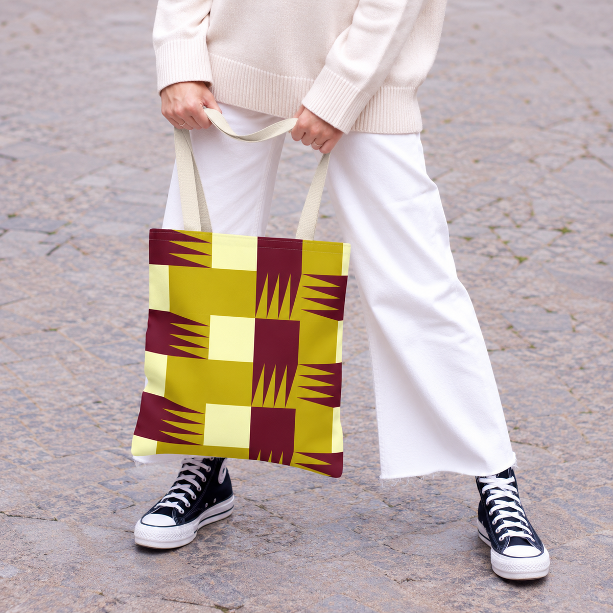 Model in white trousers holding the mustard burgundy geometric tote bag