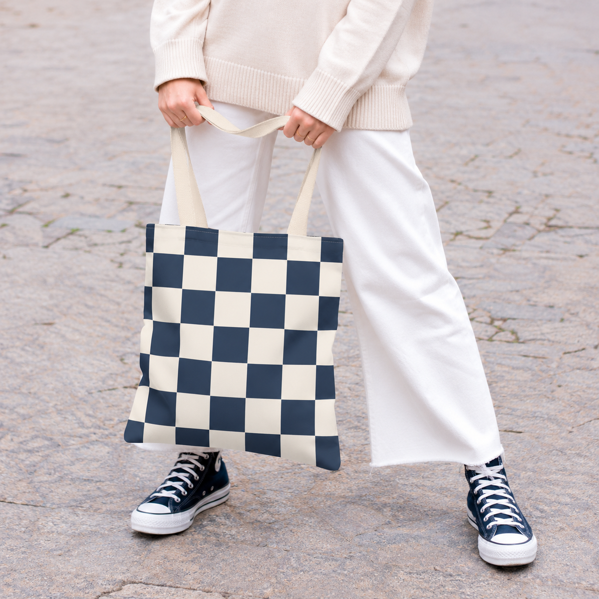 Woman in white trousers holding the navy cream checkered tote bag by the handles