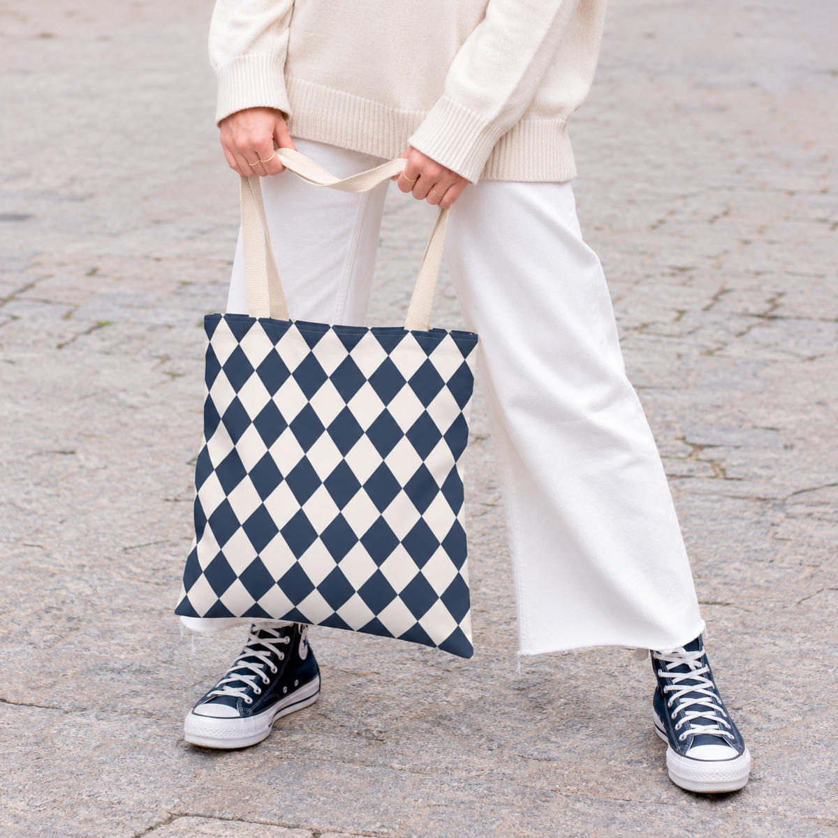 Woman holding a navy cream diamond checkered tote bag with white trousers and sneakers
