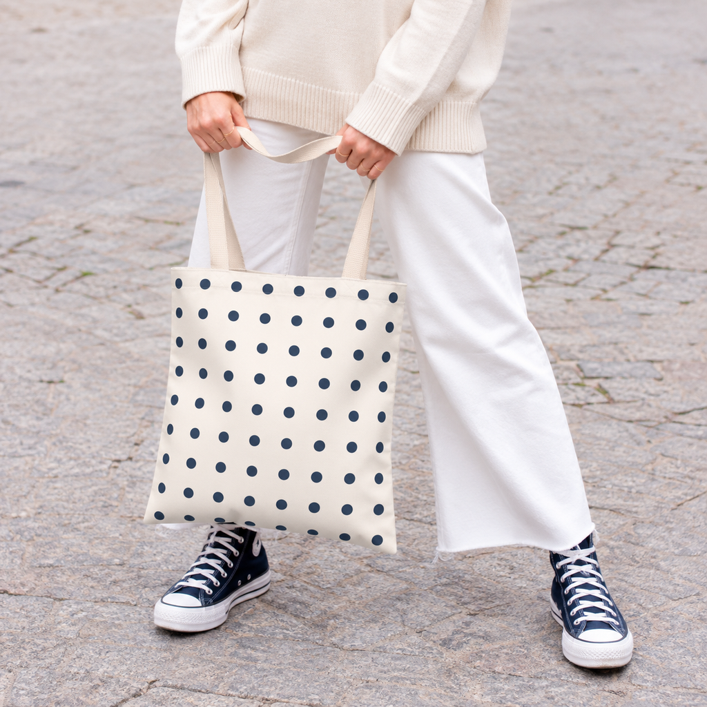 Woman holding the cream tote bag with small navy polka dots in front of her on a street