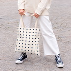 Woman holding the cream tote bag with small navy polka dots in front of her on a street