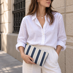 Woman in a white shirt holding the navy cream striped makeup bag as a clutch