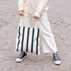 Woman in white trousers holding the navy cream striped tote bag by its handles