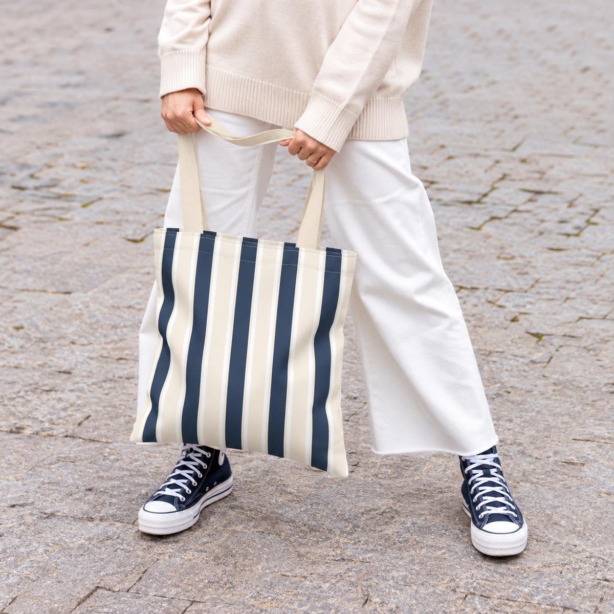 Woman in white trousers holding the navy cream striped tote bag by its handles