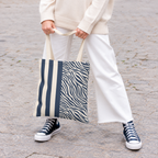 Woman holding a navy zebra striped tote bag with white trousers and sneakers