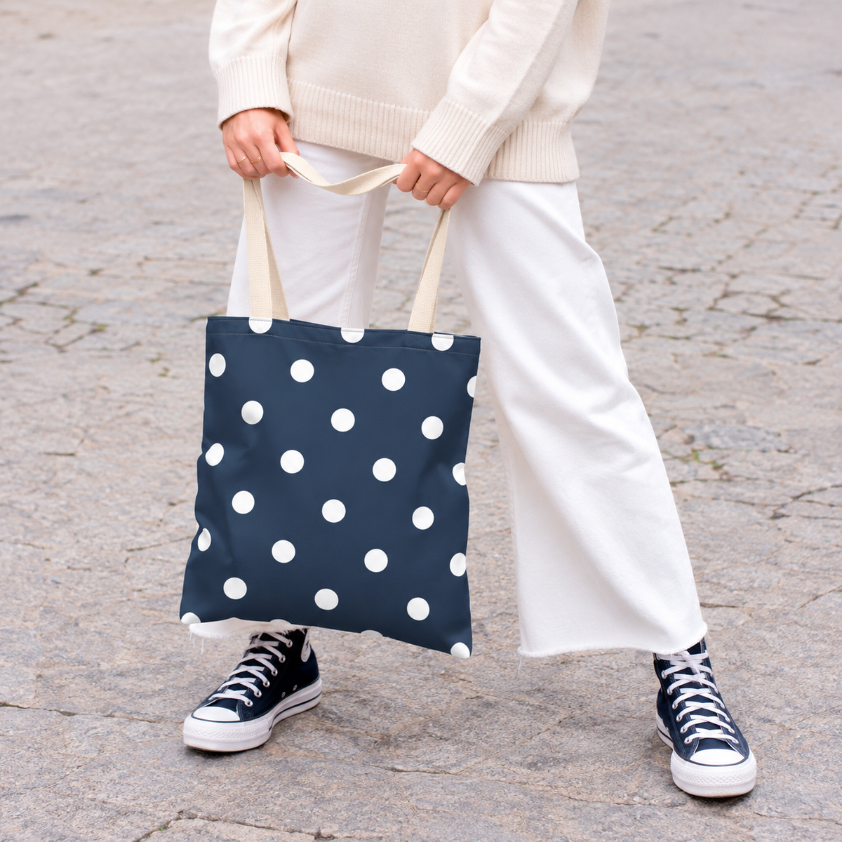 Woman holding the navy polka dot tote bag with white dots in front of her on a street