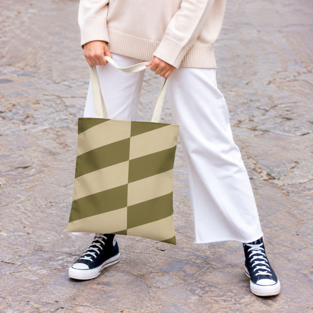 Model holding the olive beige geometric tote bag in front of white trousers
