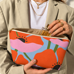 Hands holding the open orange poppy makeup bag with a perfume bottle inside