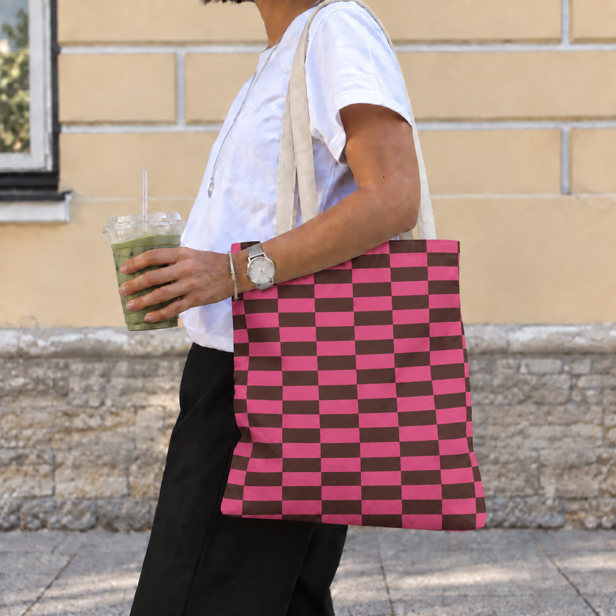 Woman carrying the pink brown checkered tote bag on her shoulder while holding a drink