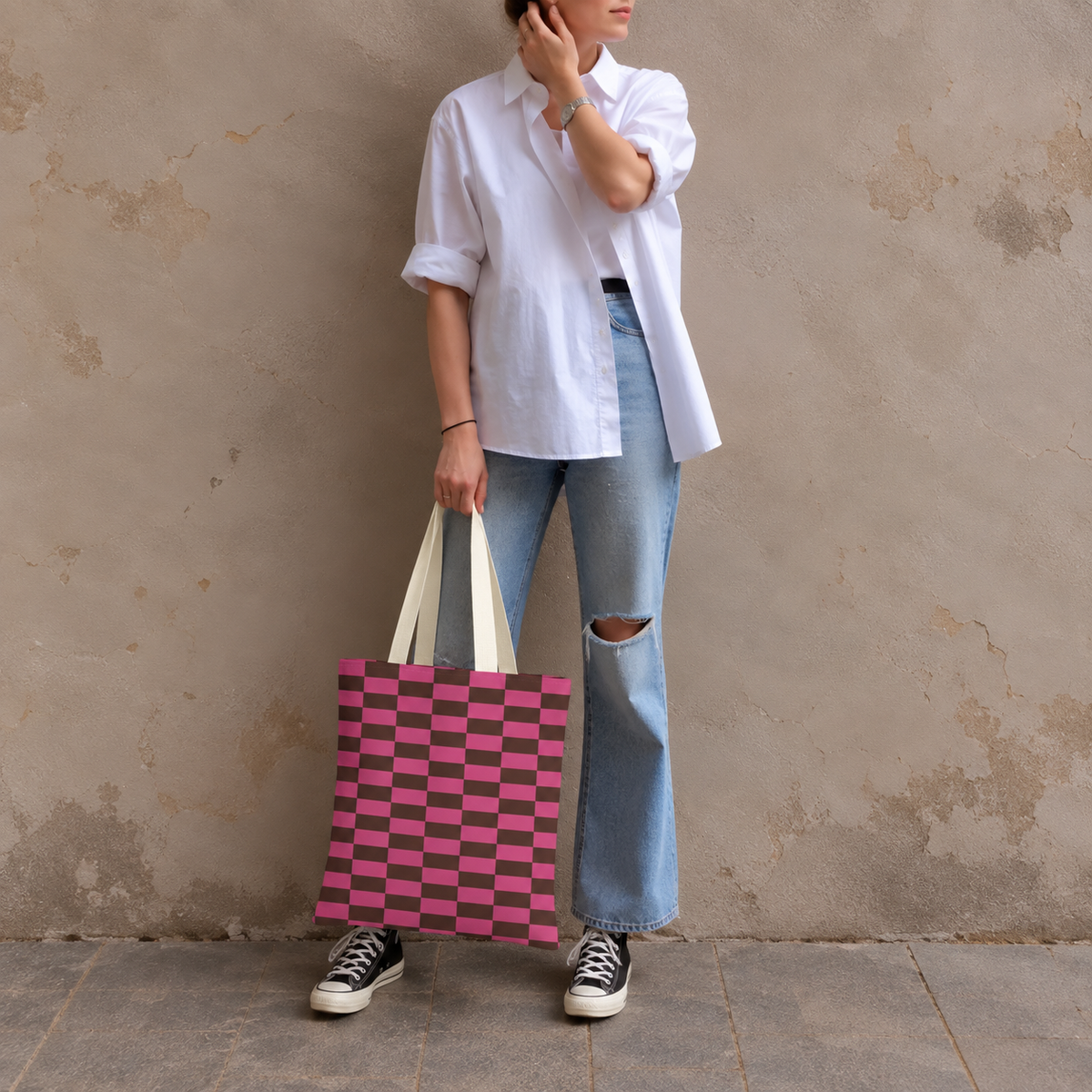 Woman standing in jeans and a white shirt with the pink brown checkered tote bag