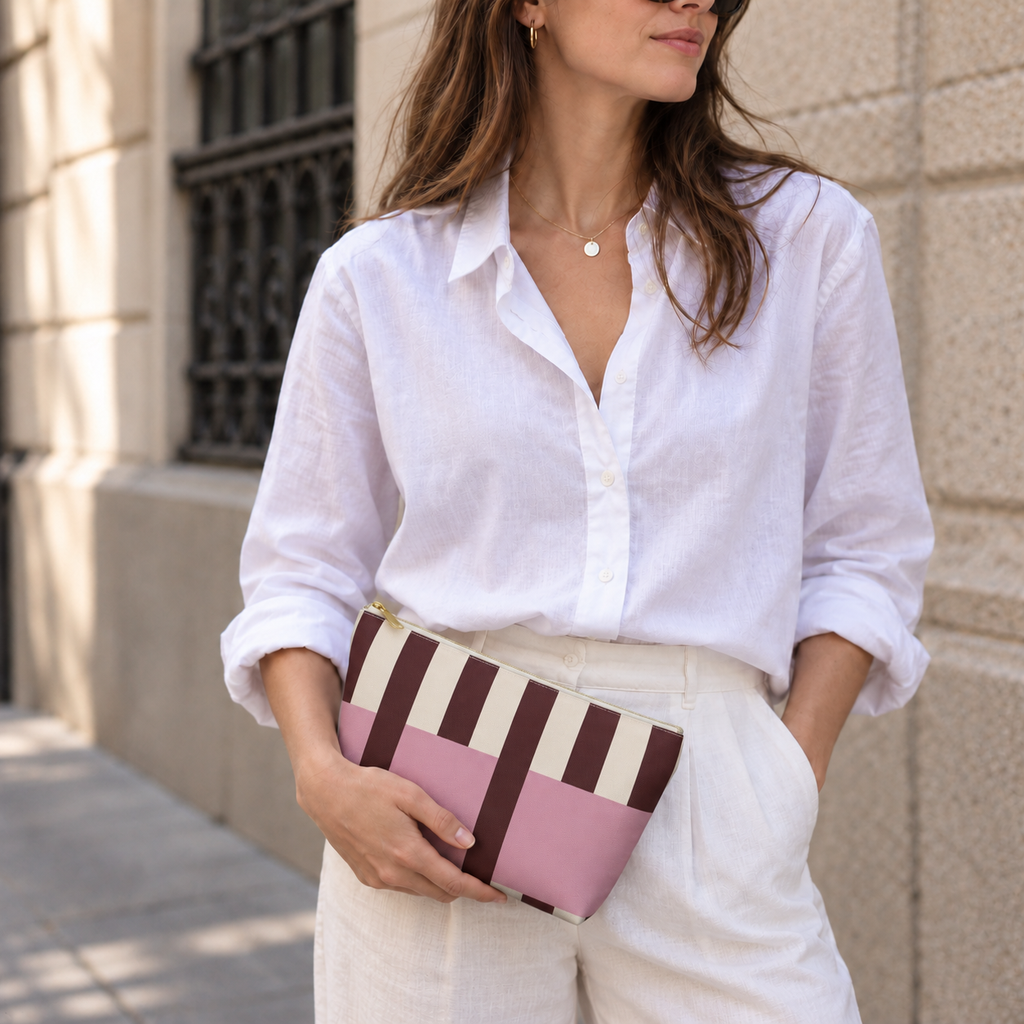 Model in a white shirt holding the pink burgundy cream striped makeup bag as a clutch