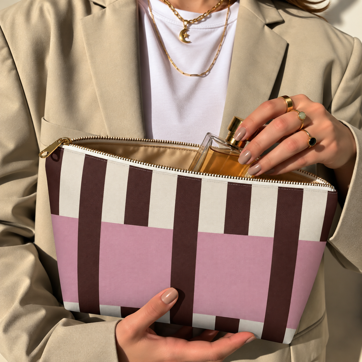 Model in a beige blazer taking a product out of the open pink burgundy cream striped makeup bag