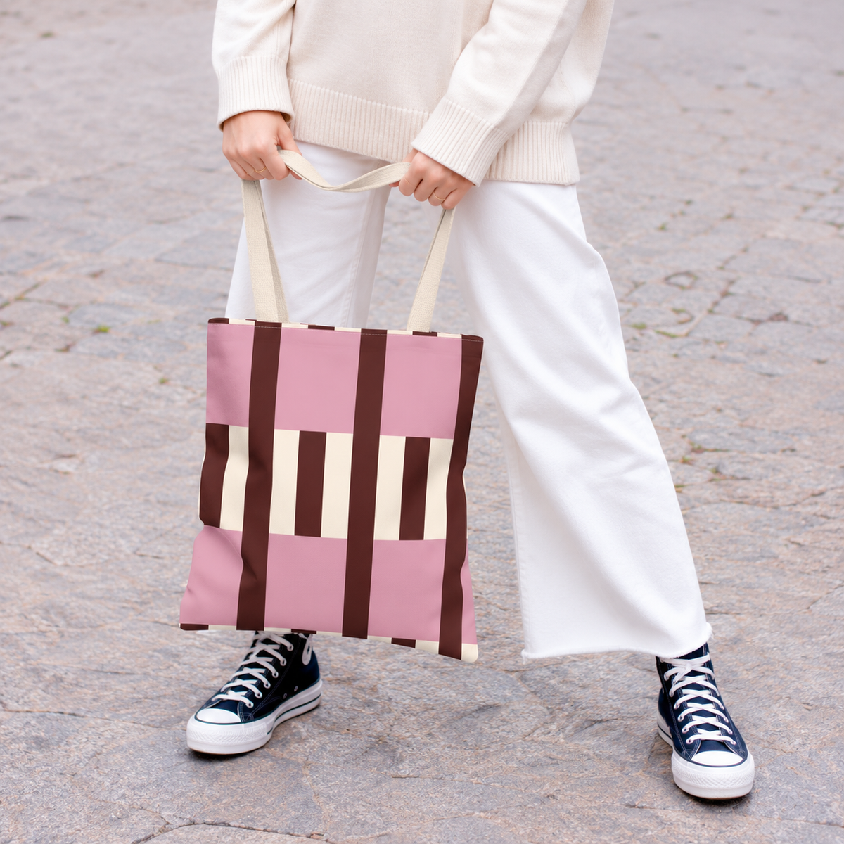 Model holding the pink burgundy cream striped tote bag in front of white trousers