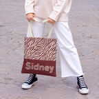 Model with white trousers holding the pink burgundy zebra print personalized tote bag