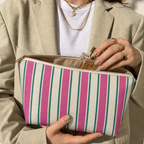 Hands holding the open Pink Green Cream Striped makeup bag filled with cosmetics