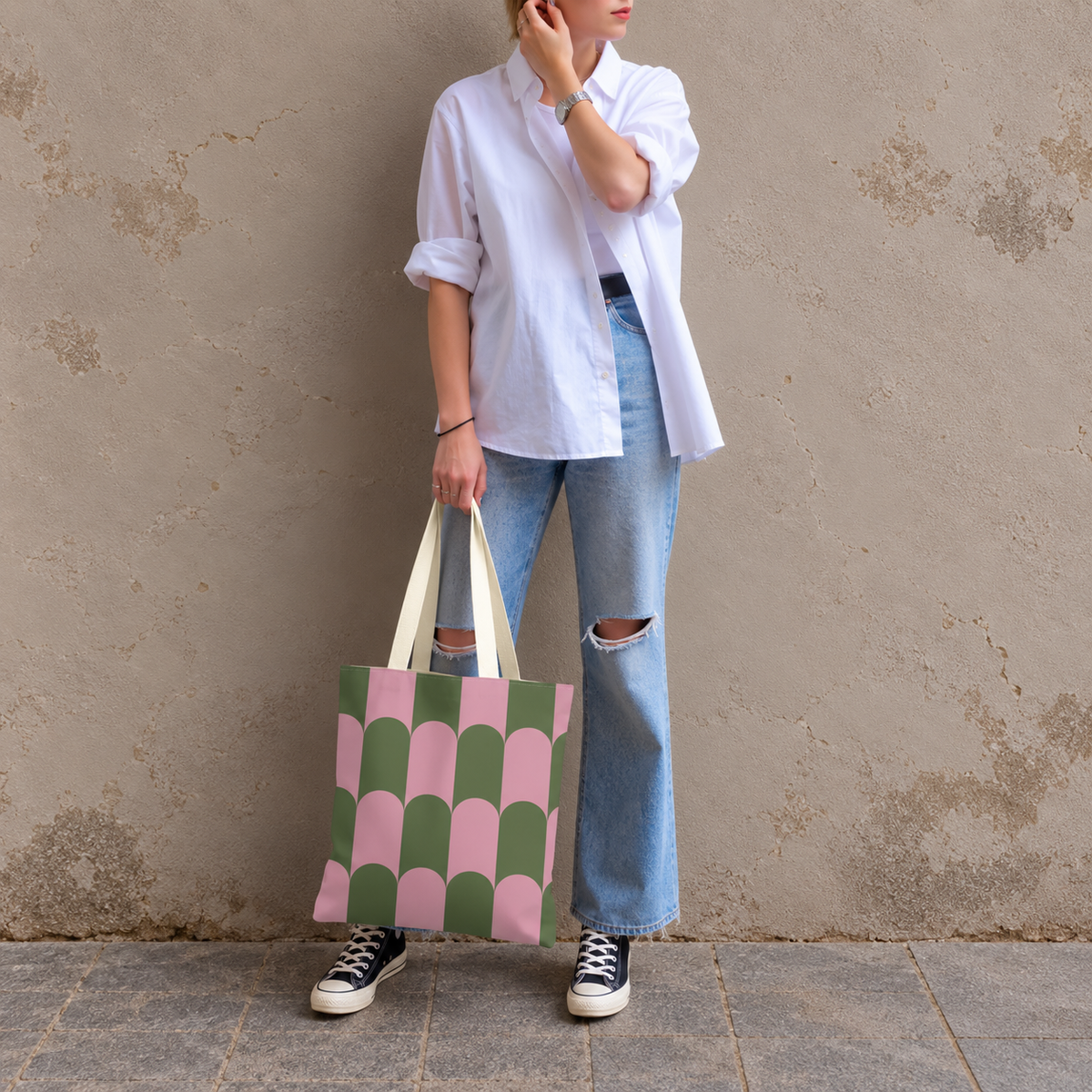 Model in jeans and a white shirt standing with the pink green scallop tote bag