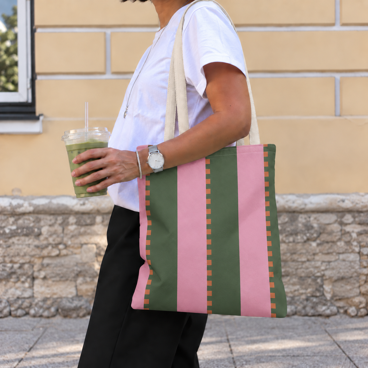 Pink green striped tote bag worn on the shoulder with an iced drink