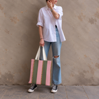 Woman in white shirt and jeans holding the pink green striped tote bag