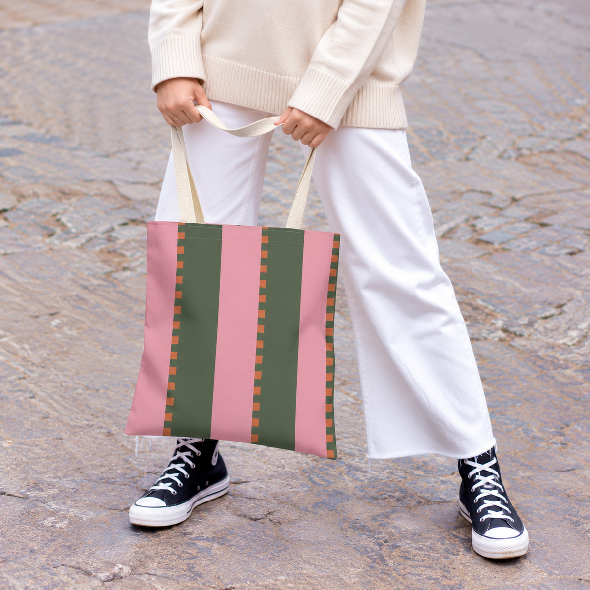 Model with white trousers holding the pink green striped tote bag