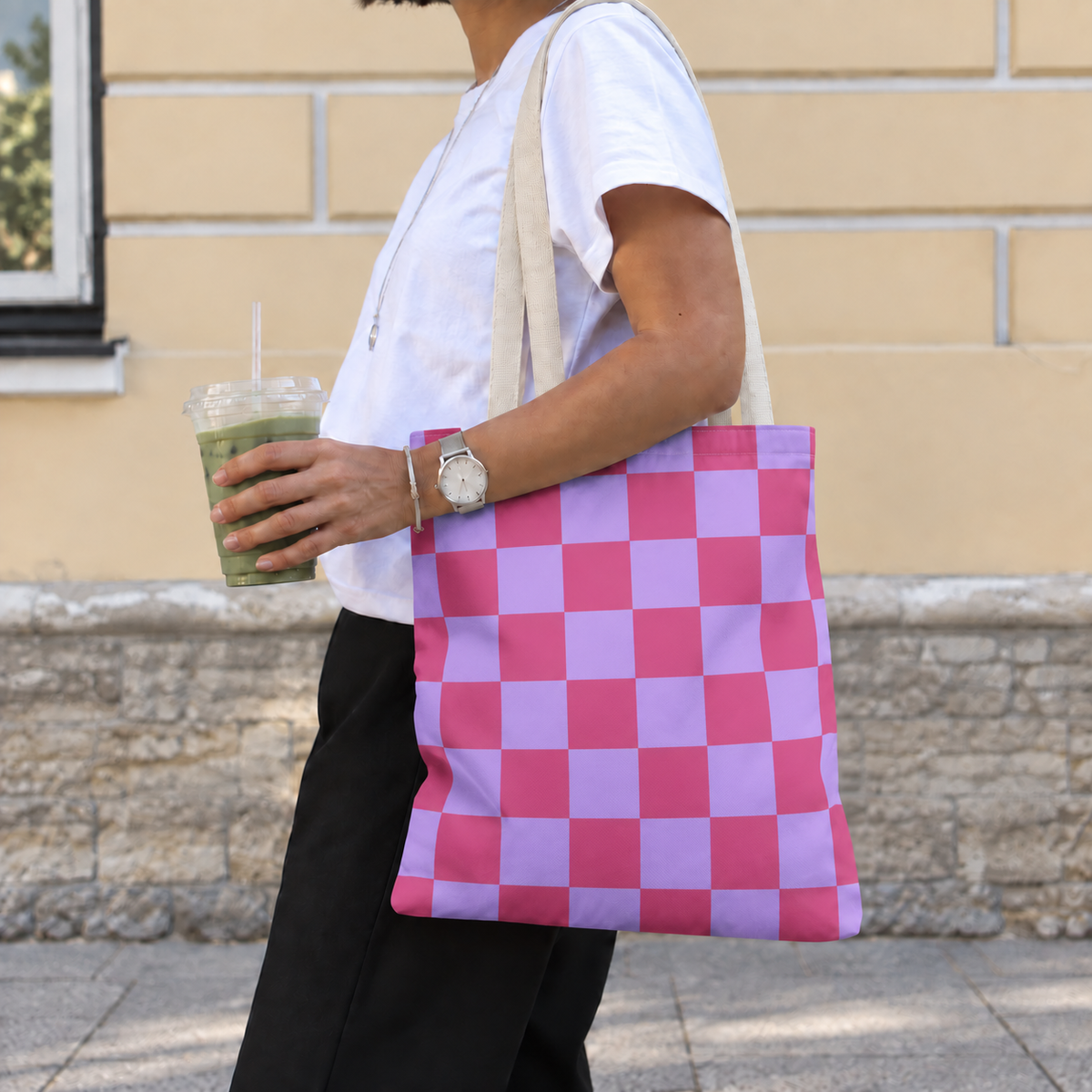 Woman carrying the pink purple checkered tote bag on her shoulder while holding a drink