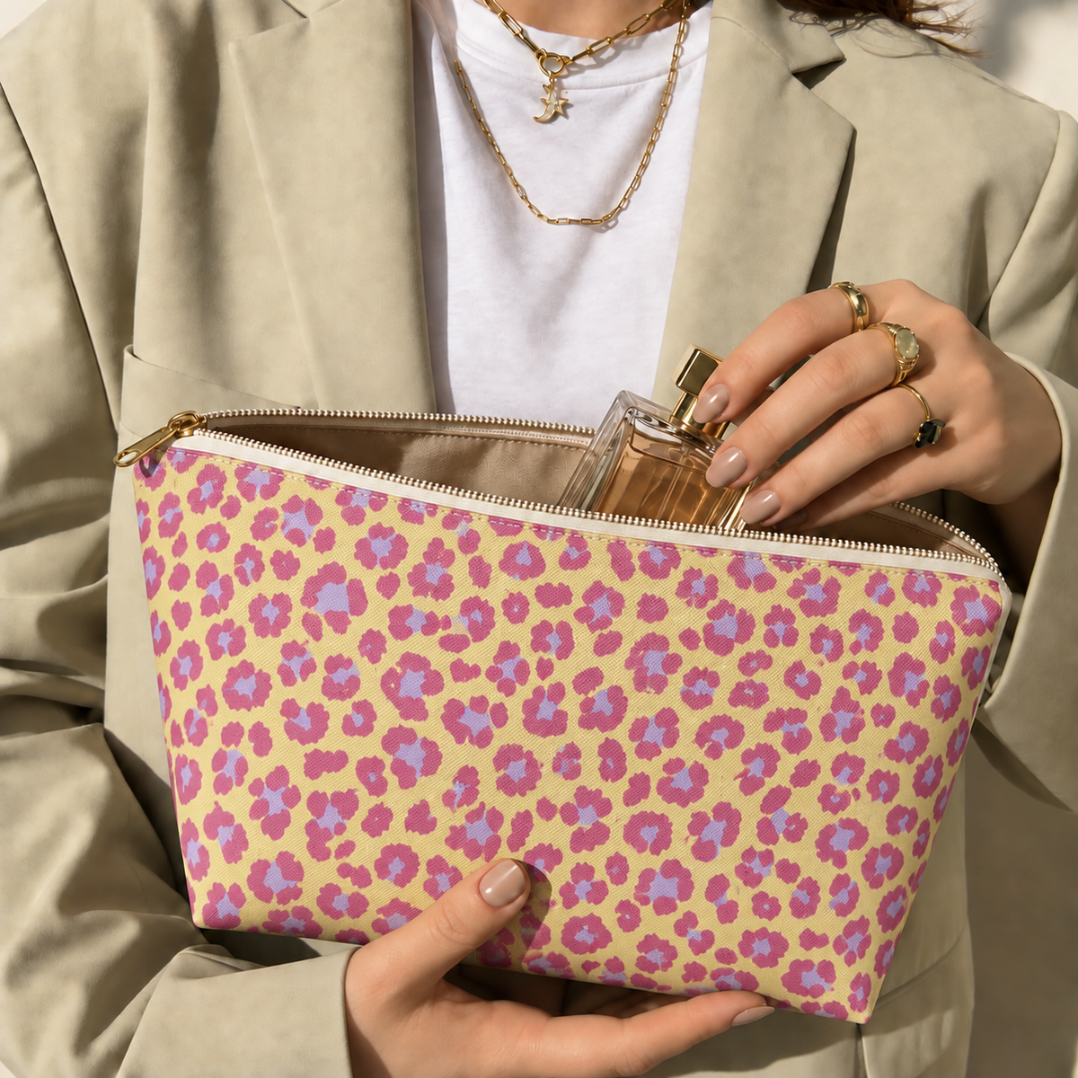 Hands holding the pink purple leopard print makeup bag with a perfume bottle inside