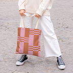 Model holding the pink terracotta color block tote bag in front of white trousers