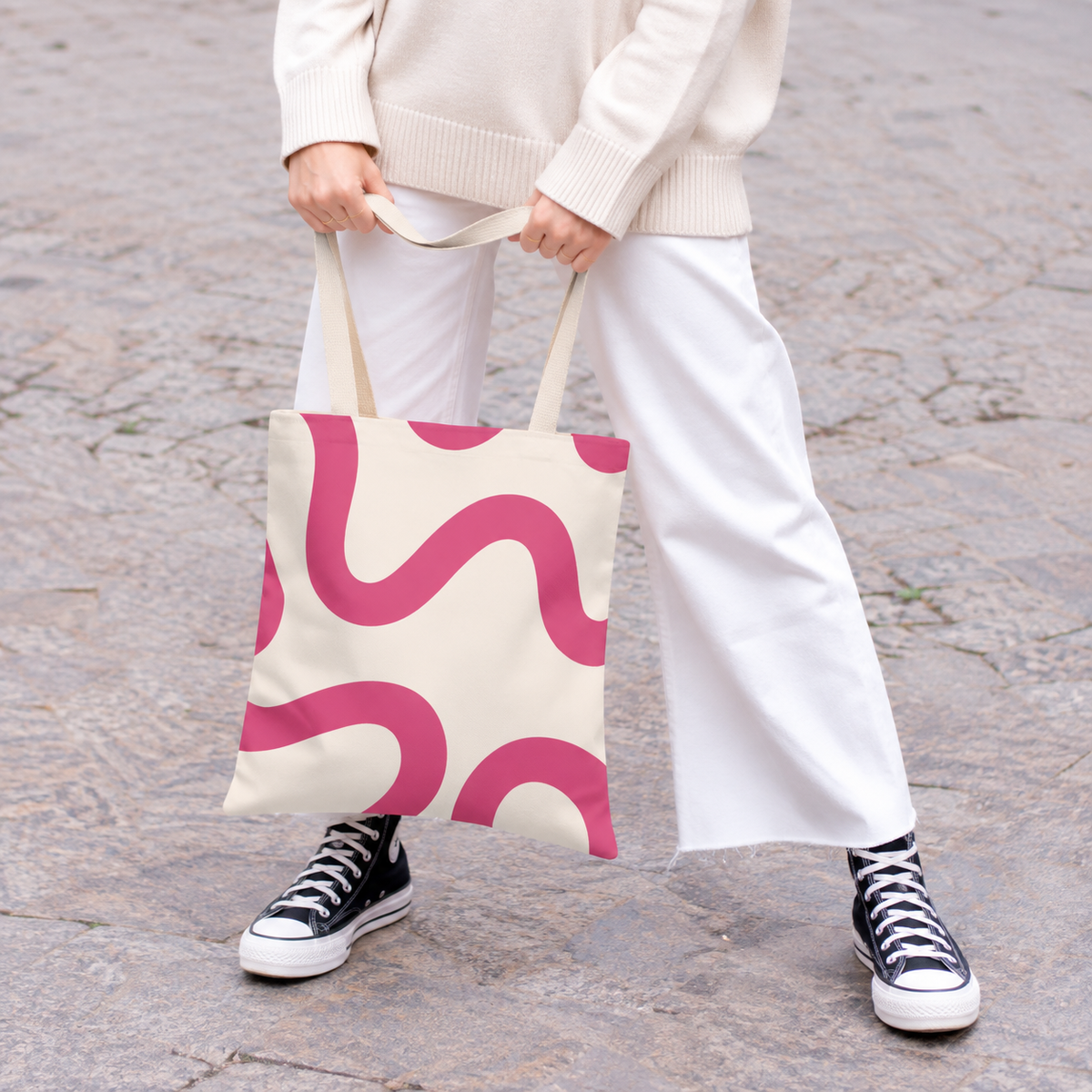 Woman in white trousers holding the pink wavy line tote bag by the handles