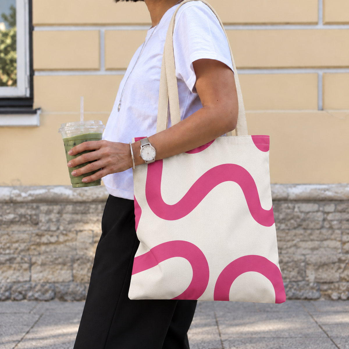 Woman carrying the pink wavy line tote bag on her shoulder while holding a drink