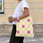 Woman carrying the pink yellow smiley checkered tote bag on her shoulder while holding a drink
