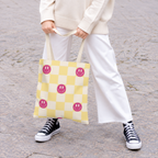 Woman in white trousers holding the pink yellow smiley checkered tote bag by the handles