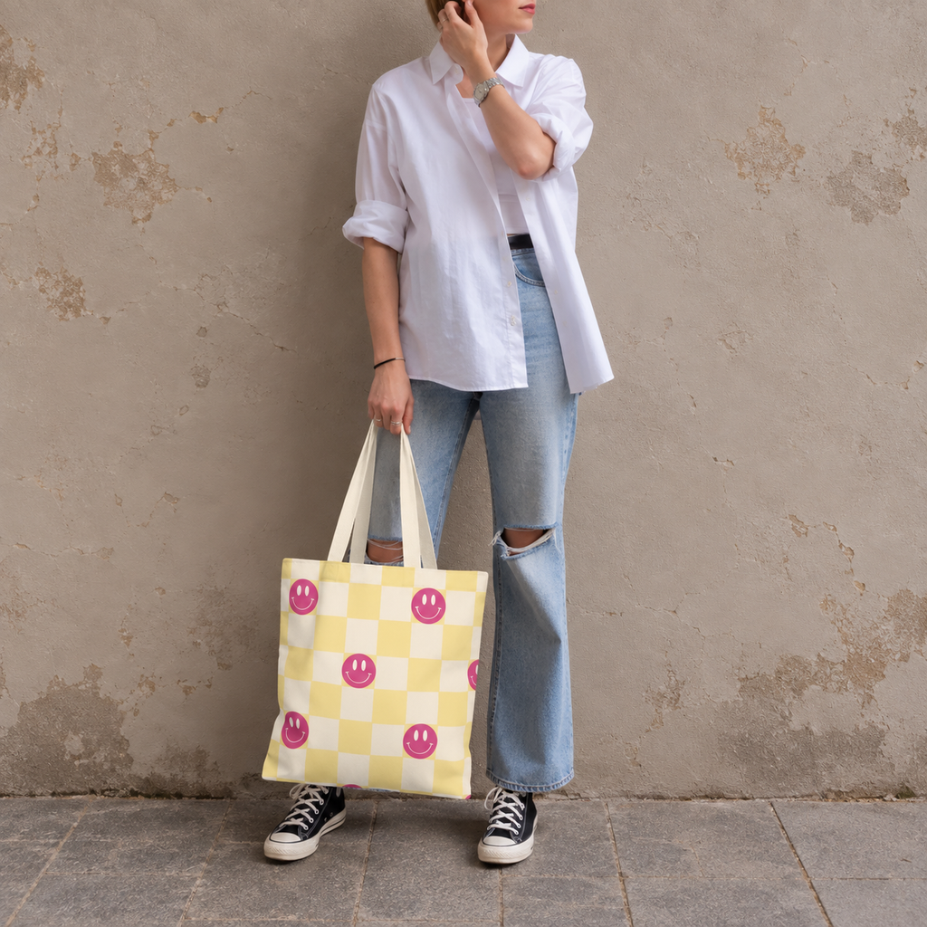 Woman standing in jeans and a white shirt with the pink yellow smiley checkered tote bag