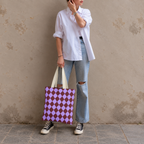 Woman in jeans and sneakers holding the purple burgundy diamond checkered tote bag